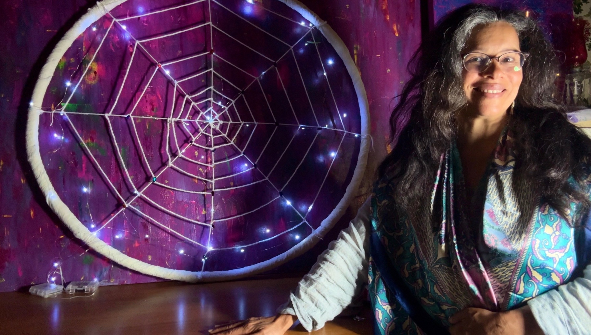 Reverent Mariela beside a large lit web of white cord and fairy lights