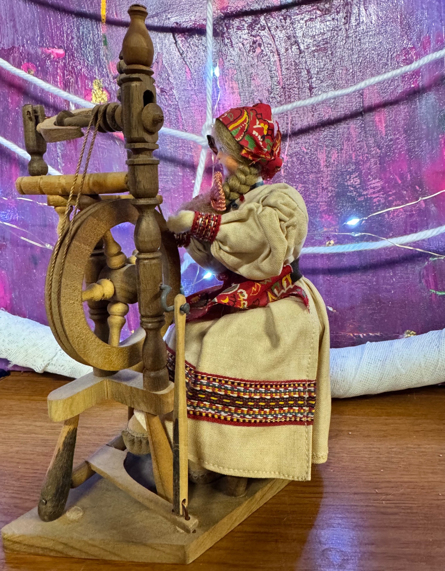 A wooden doll at a spinning wheel before a violet lit web